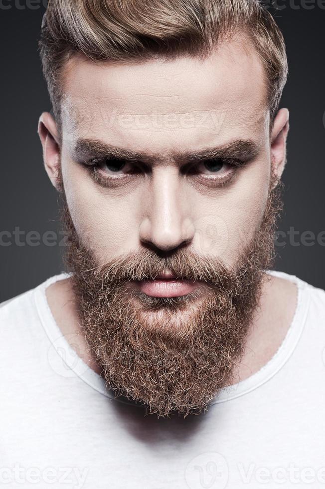 retrato de la masculinidad. retrato de un apuesto joven barbudo mirando a la cámara mientras se enfrenta a un fondo gris foto