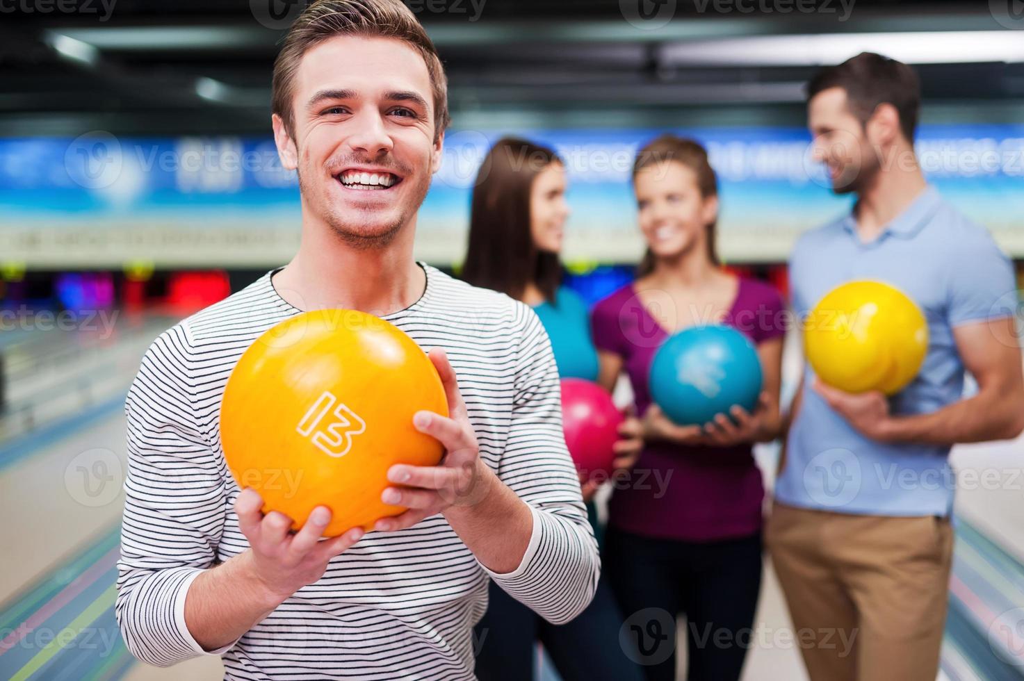 The best player. Handsome young men holding a bowling ball while three people communicating against bowling alleys photo