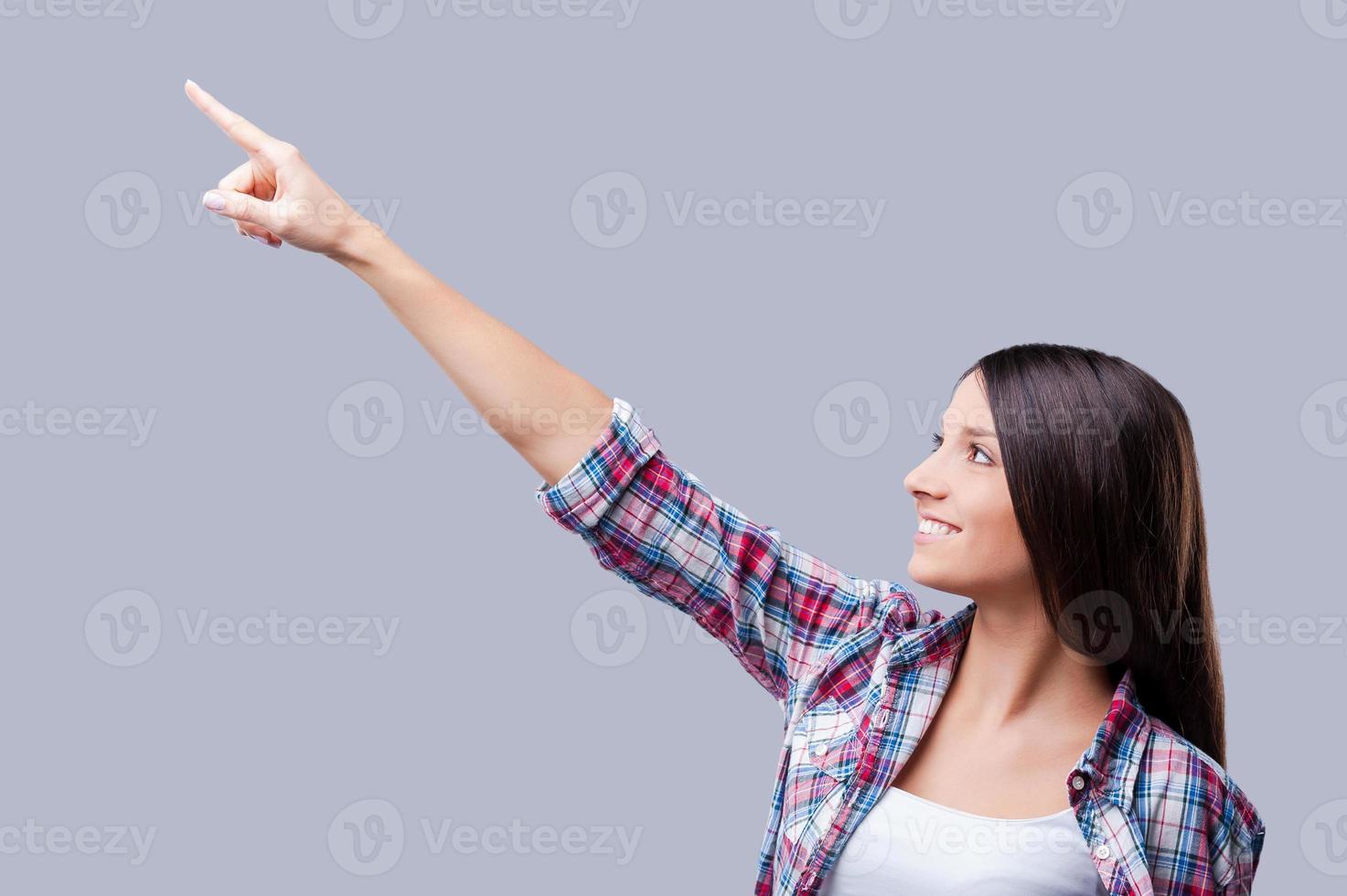 lo que hay encima una joven sonriente señalando hacia otro lado mientras se enfrenta a un fondo gris foto