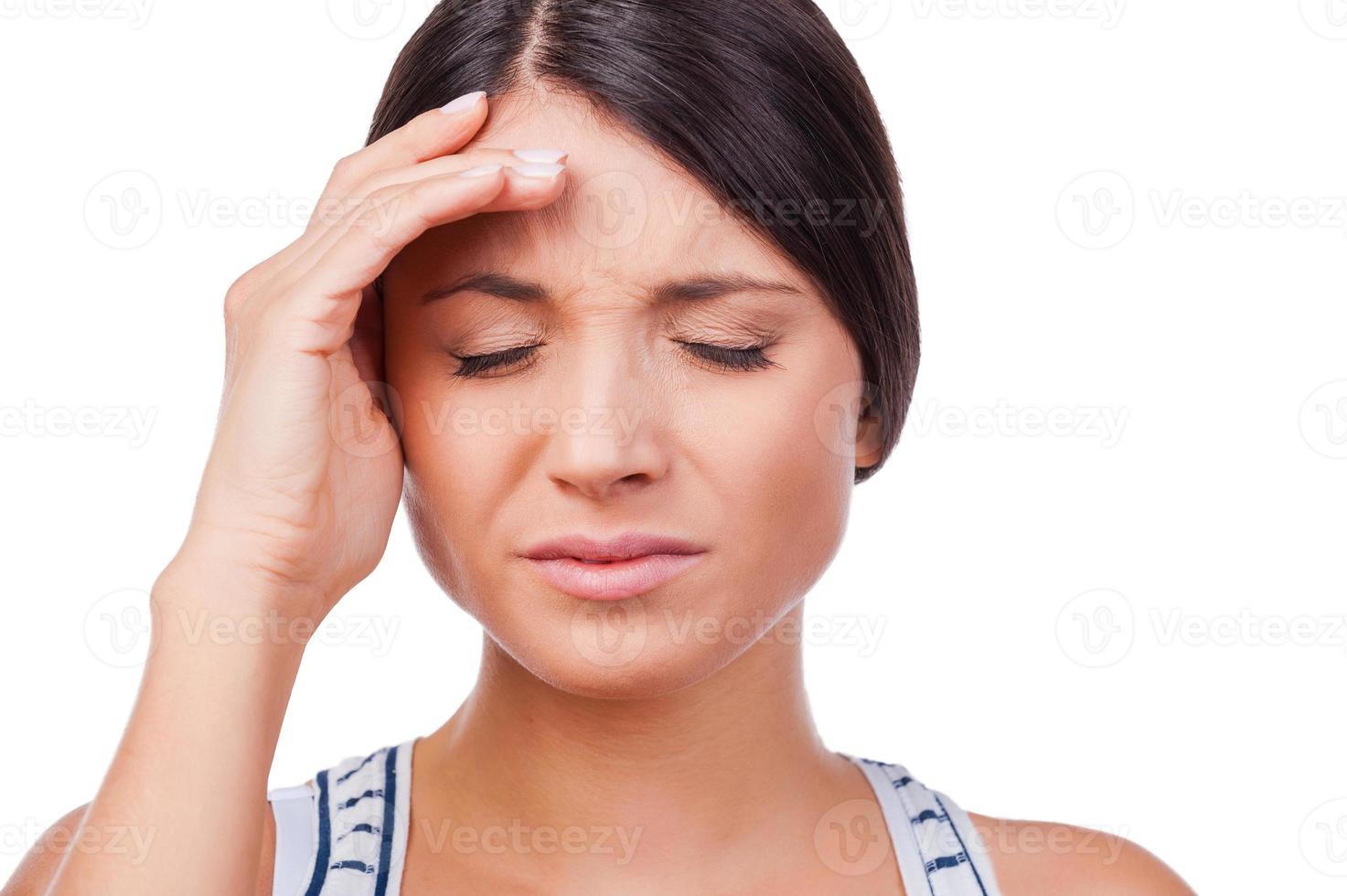 Suffering from migraine. Depressed young woman holding a hand on forehead while standing against white background photo