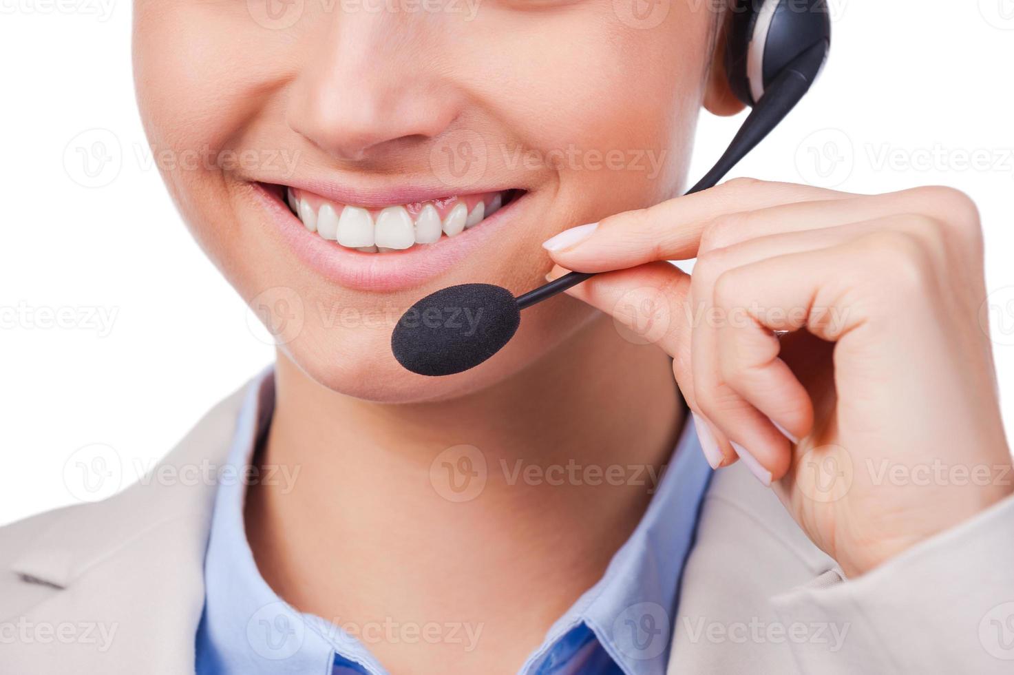 ¿Cómo puedo ayudarlo? Primer plano de una joven representante de servicio al cliente ajustando sus auriculares y sonriendo mientras está de pie contra un fondo blanco foto