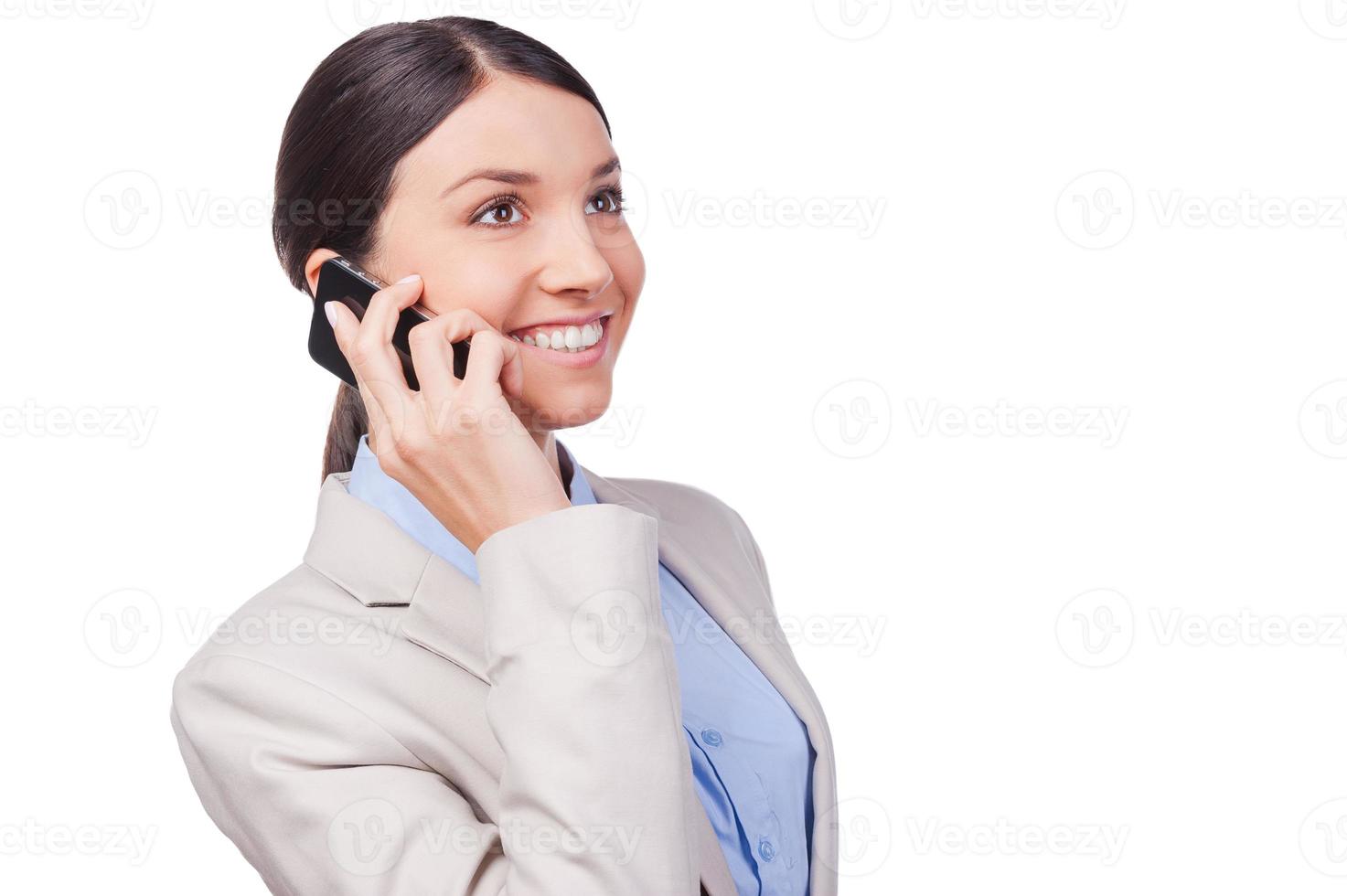 Business talk. Beautiful young businesswoman talking on the mobile phone and smiling while standing against white background photo