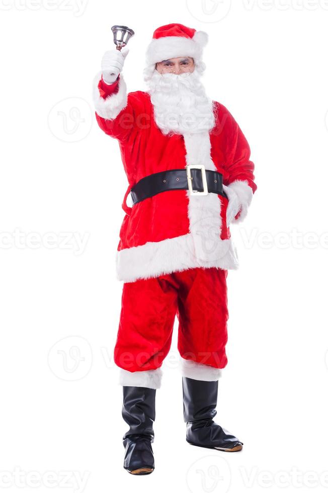 Merry Christmas to you Traditional Santa Claus ringing a bell and looking at camera while standing against white background photo