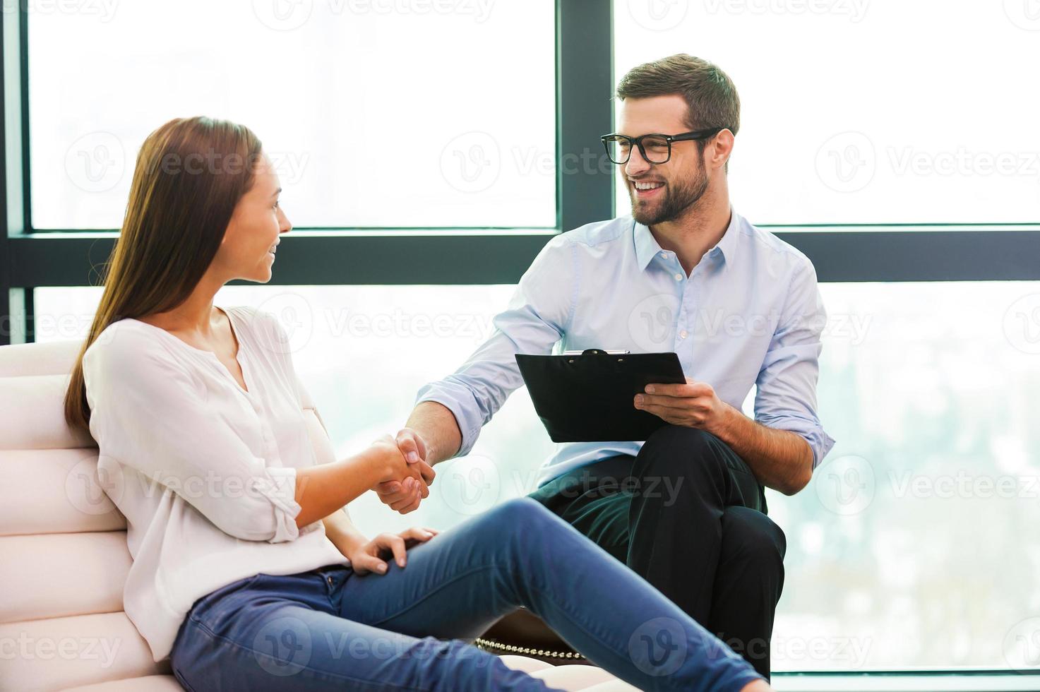 Thank you doctor Cheerful male psychiatrist shaking hand to beautiful young woman sitting close to him photo