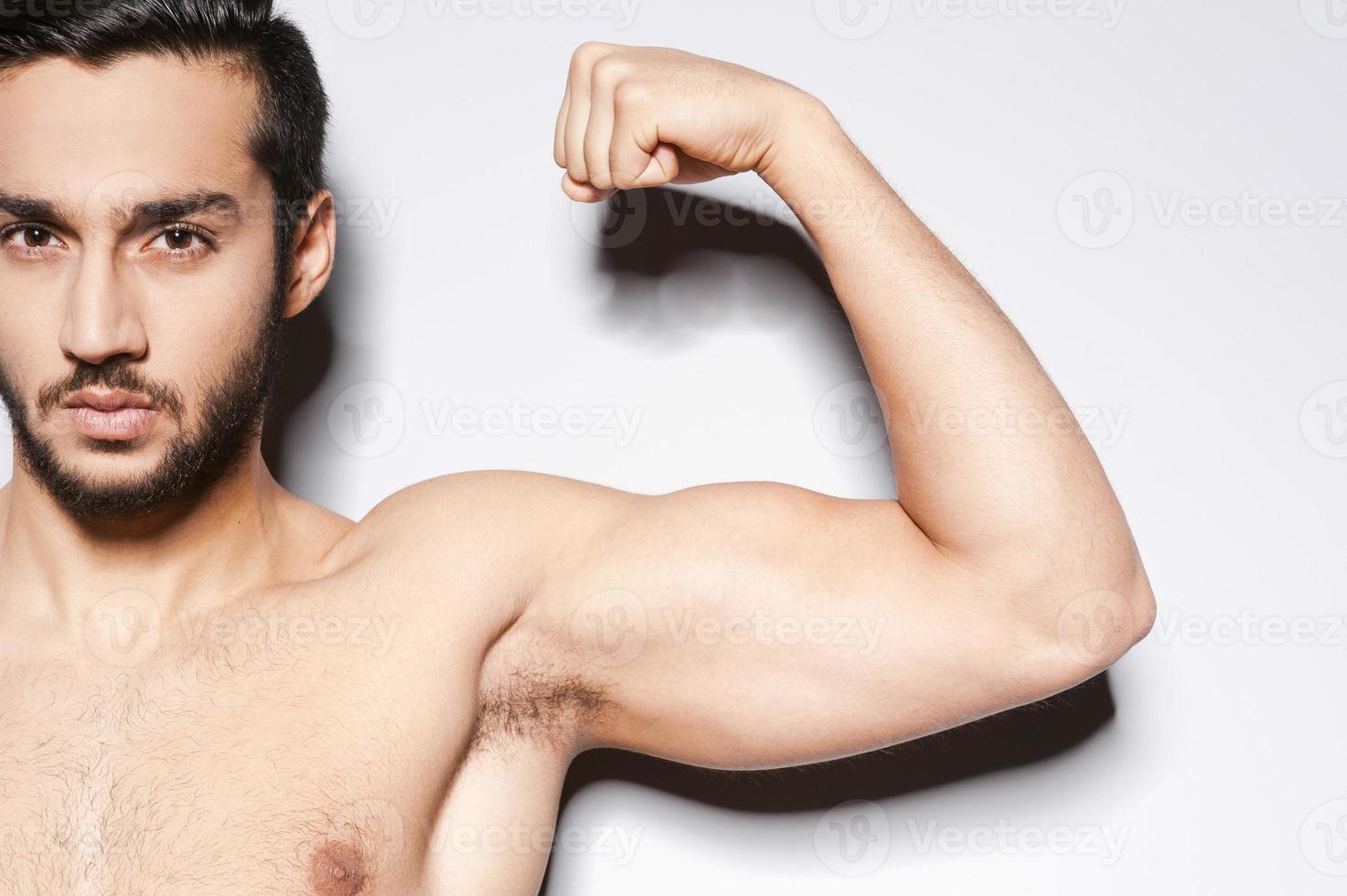 Perfect bicep. Close-up of muscular man showing his perfect bicep while standing against grey background photo