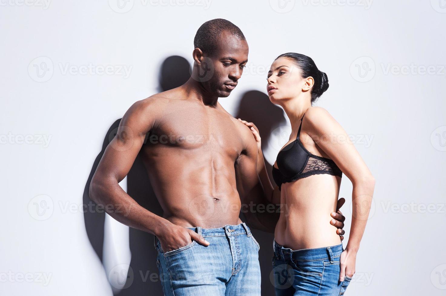 In denim style. Beautiful young couple in jeans bonding to each other while both standing against grey background photo