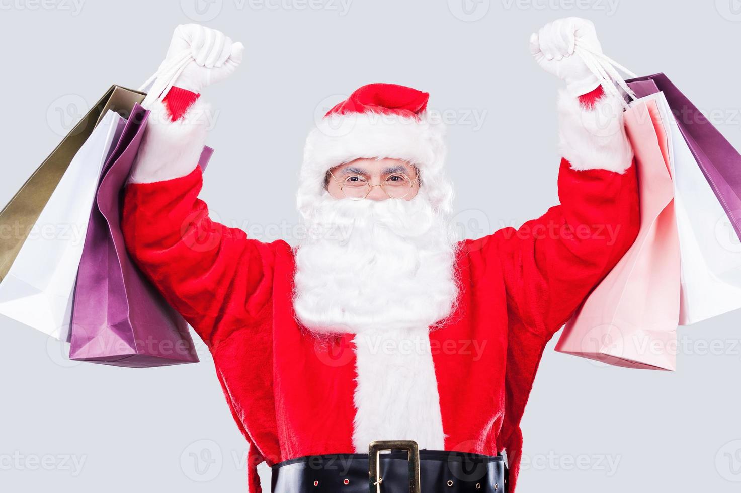 ventas de navidad feliz santa claus sosteniendo bolsas de compras mientras está de pie contra el fondo gris foto