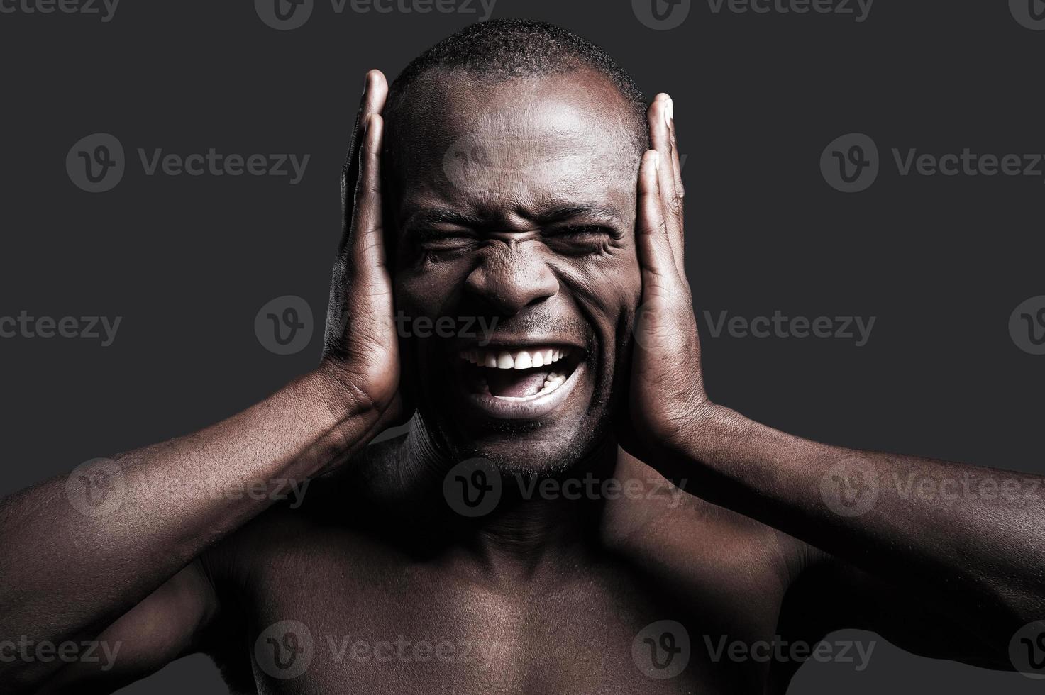 Too loud sound. Portrait of young shirtless African man covering ears