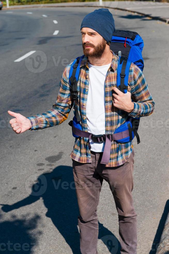 recogiendo un joven apuesto que lleva una mochila estirando la mano con el pulgar hacia arriba mientras está de pie en la carretera foto