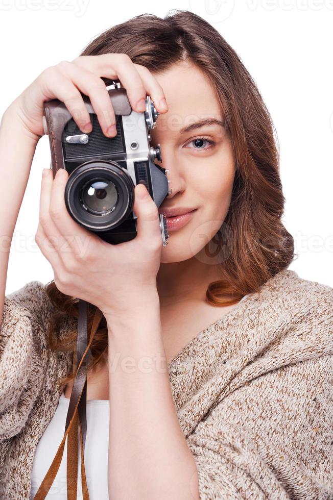 Smile to a camera Attractive young woman photographing you with her old-fashioned camera while standing isolated on white photo