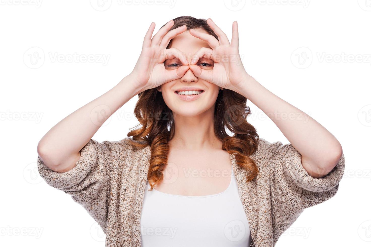 belleza juguetona. juguetona joven mujer sonriente mirando a la cámara y sonriendo mientras sostiene los dedos cerca de los ojos y se encuentra aislada en blanco foto