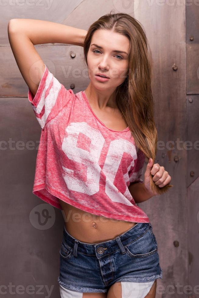 She knows that she is perfect. Beautiful young woman in posing and looking at camera while standing against metal background photo