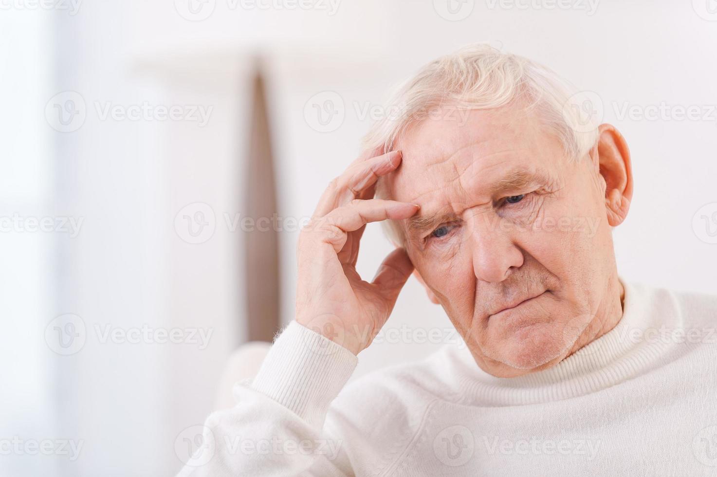 Worried senior man. Frustrated senior man touching his head while sitting in chair photo