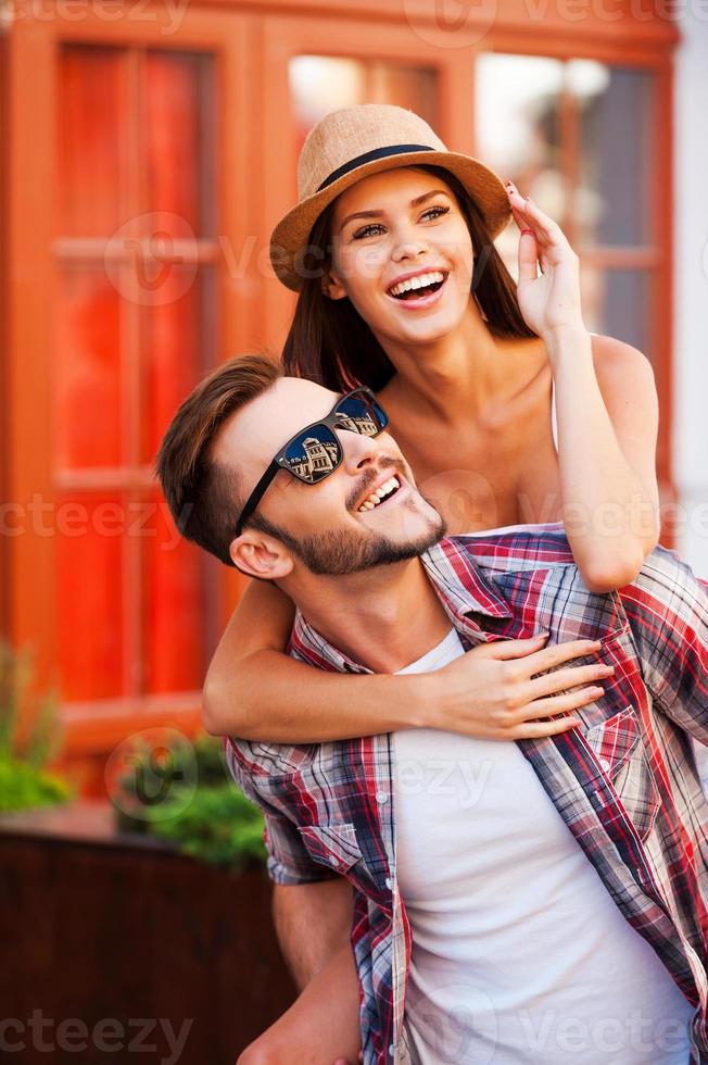 feliz pareja amorosa. joven feliz cargando a su hermosa novia sobre los hombros y sonriendo mientras camina por la calle foto