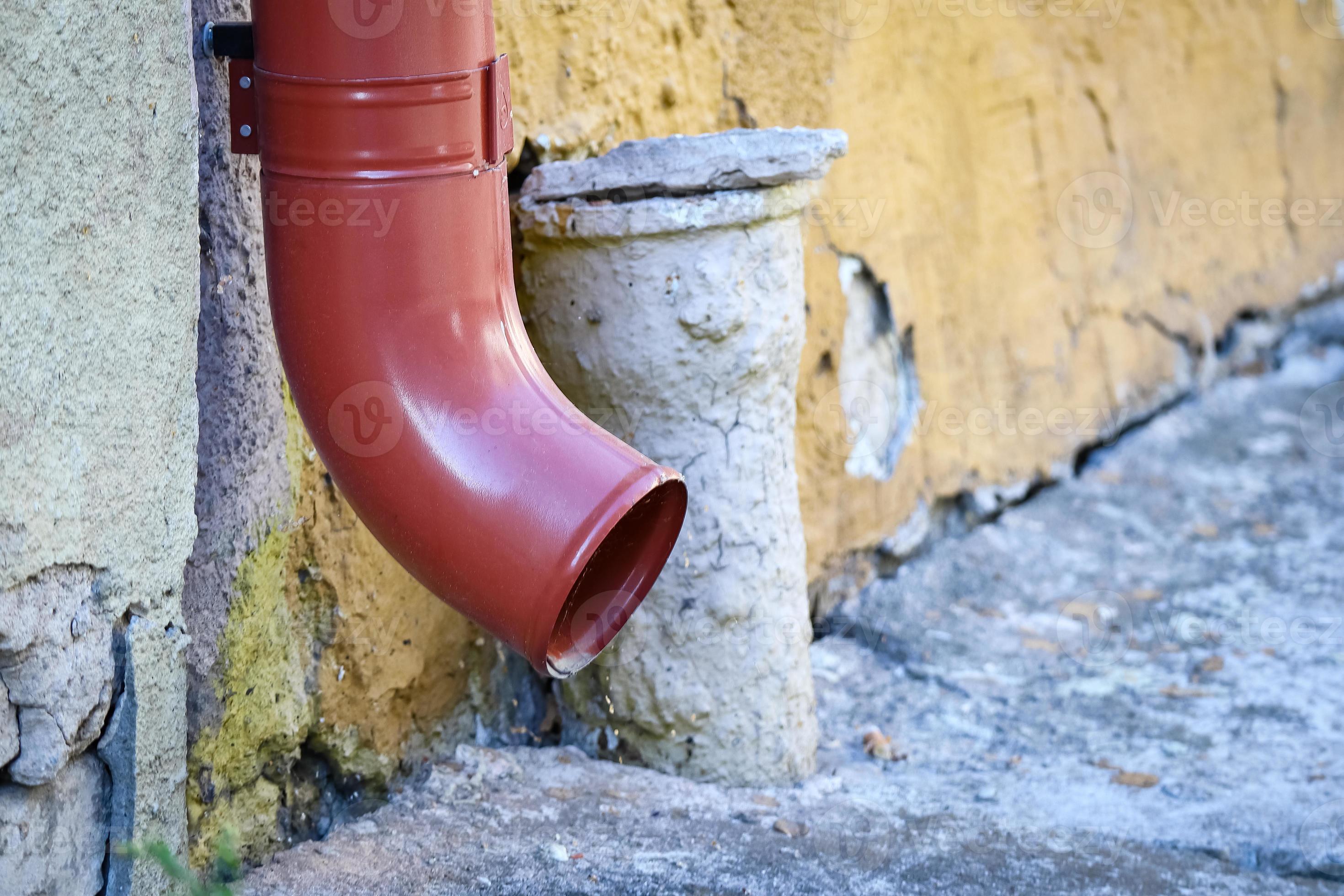Red water drain on a street of a small city pavement near yellow wall ...
