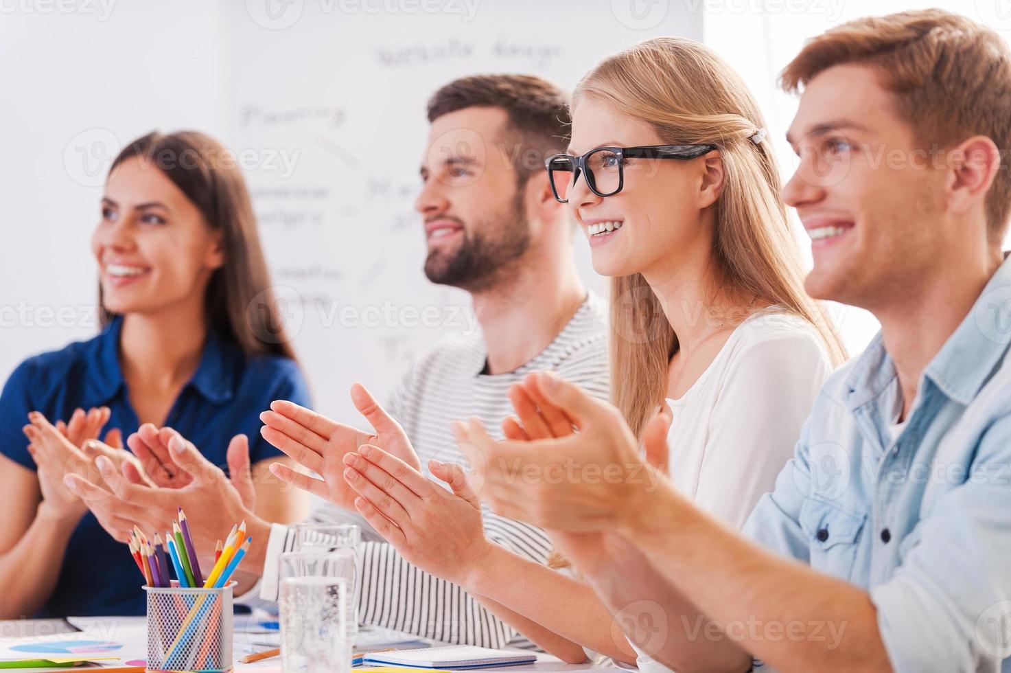 Great presentation Group of happy business people in smart casual wear sitting together at the table and applauding to someone photo