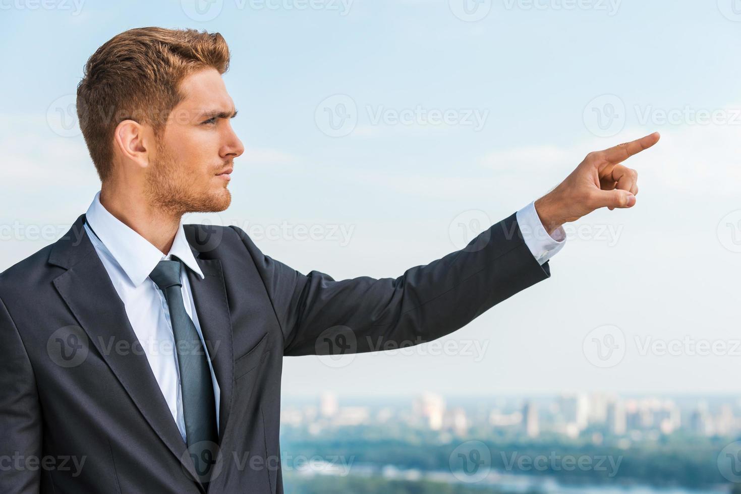 hombre de negocios apuntando hacia otro lado. un joven seguro de sí mismo con ropa formal señalando mientras está de pie al aire libre con el paisaje urbano en el fondo foto