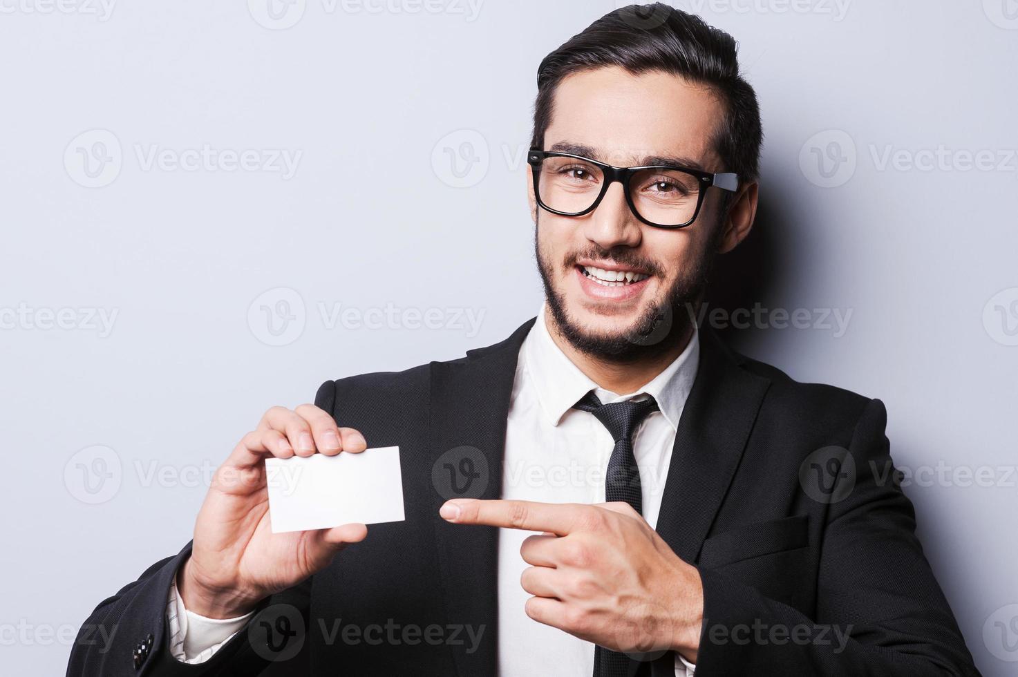 todo este número de un joven apuesto con ropa formal estirando una tarjeta de visita mientras se enfrenta a un fondo gris foto