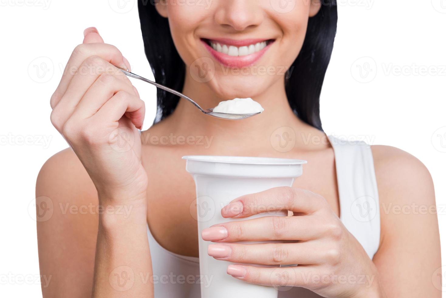 My special breakfast. Close-up of young smiling woman holding a spoon with sour cream while standing against white background photo
