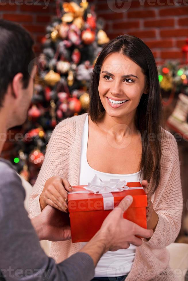 es para mí vista trasera de un joven que le da una caja de regalo roja a su novia con un árbol de navidad en el fondo foto