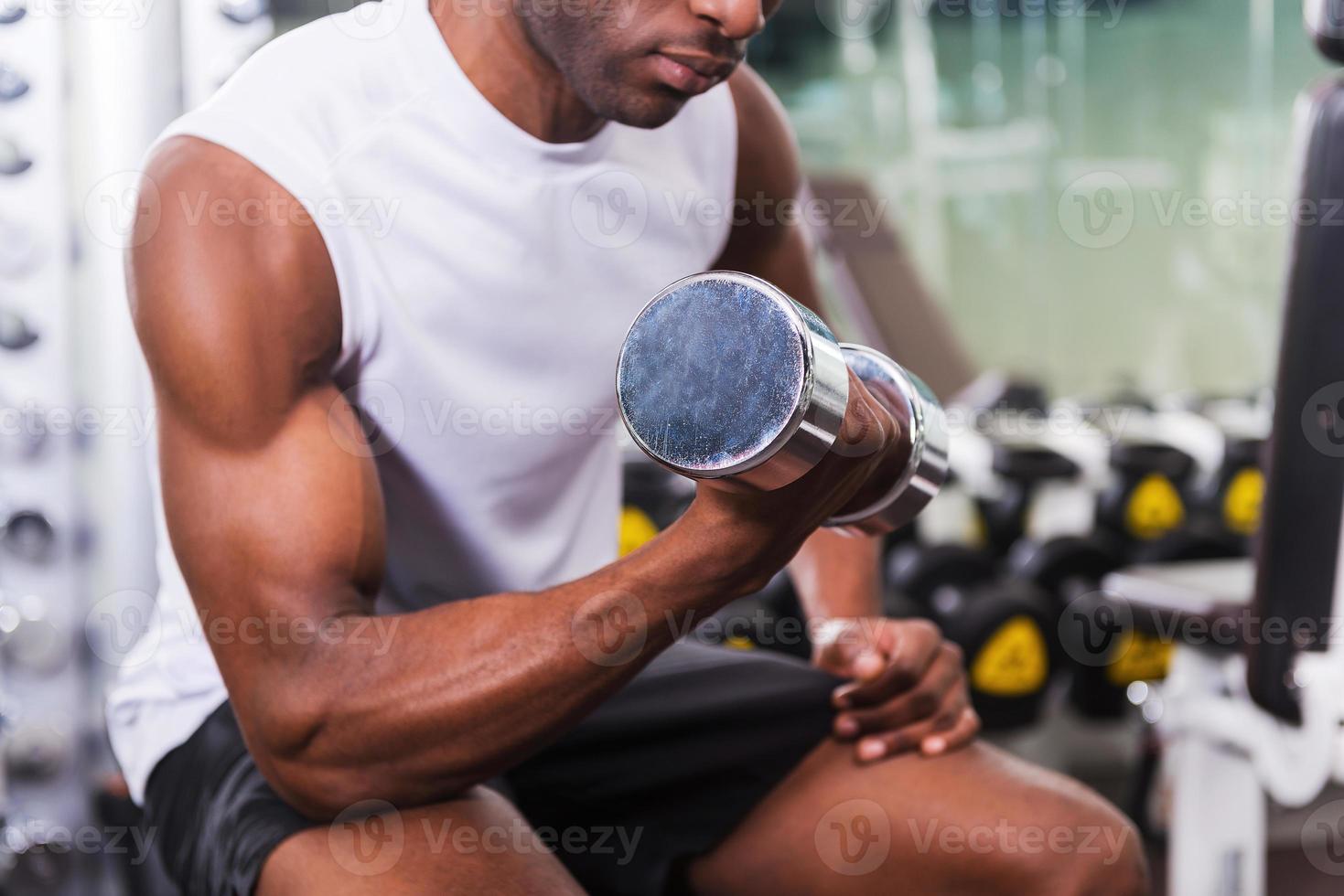 Bodybuilding. Cropped image of young African man training with dumbbell in gym photo