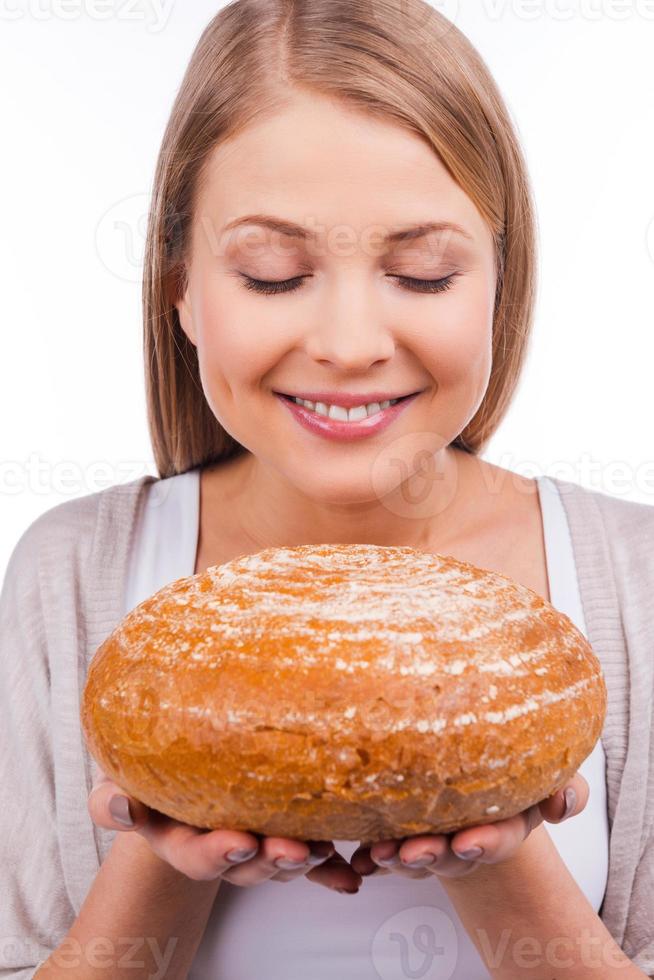 pan fresco. bella joven sosteniendo pan y oliéndolo con una sonrisa mientras se enfrenta a fondo blanco foto