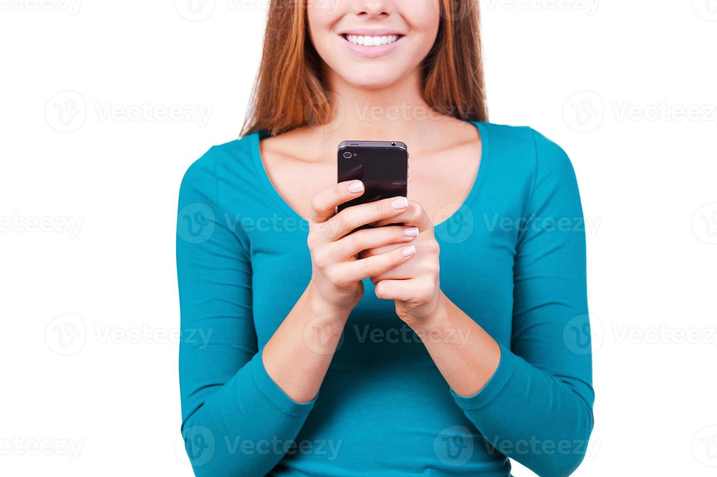 Typing a message for you. Close-up of young women talking on the mobile phone and smiling while standing against white background photo