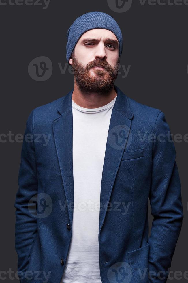 Confident and handsome. Handsome young bearded man in smart casual wear looking at camera while standing against grey background photo
