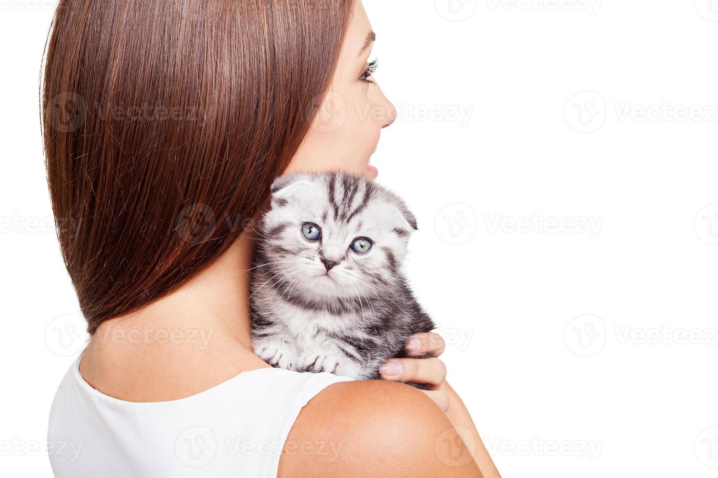 Feeling calm and protected. Beautiful young woman carrying her little kitten on shoulder and smiling while standing isolated on white background photo