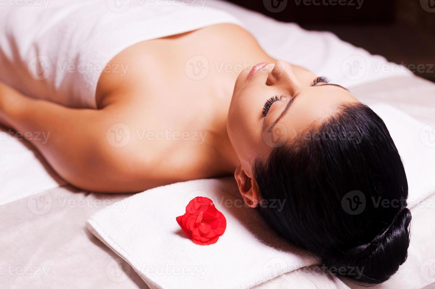 Blissful moments. Top view of beautiful young woman wrapped in towel lying on massage table and keeping eyes close photo