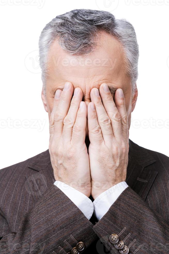 Sometimes there are situations that are out of control.  Frustrated mature man covering his face by hands while standing against white background photo