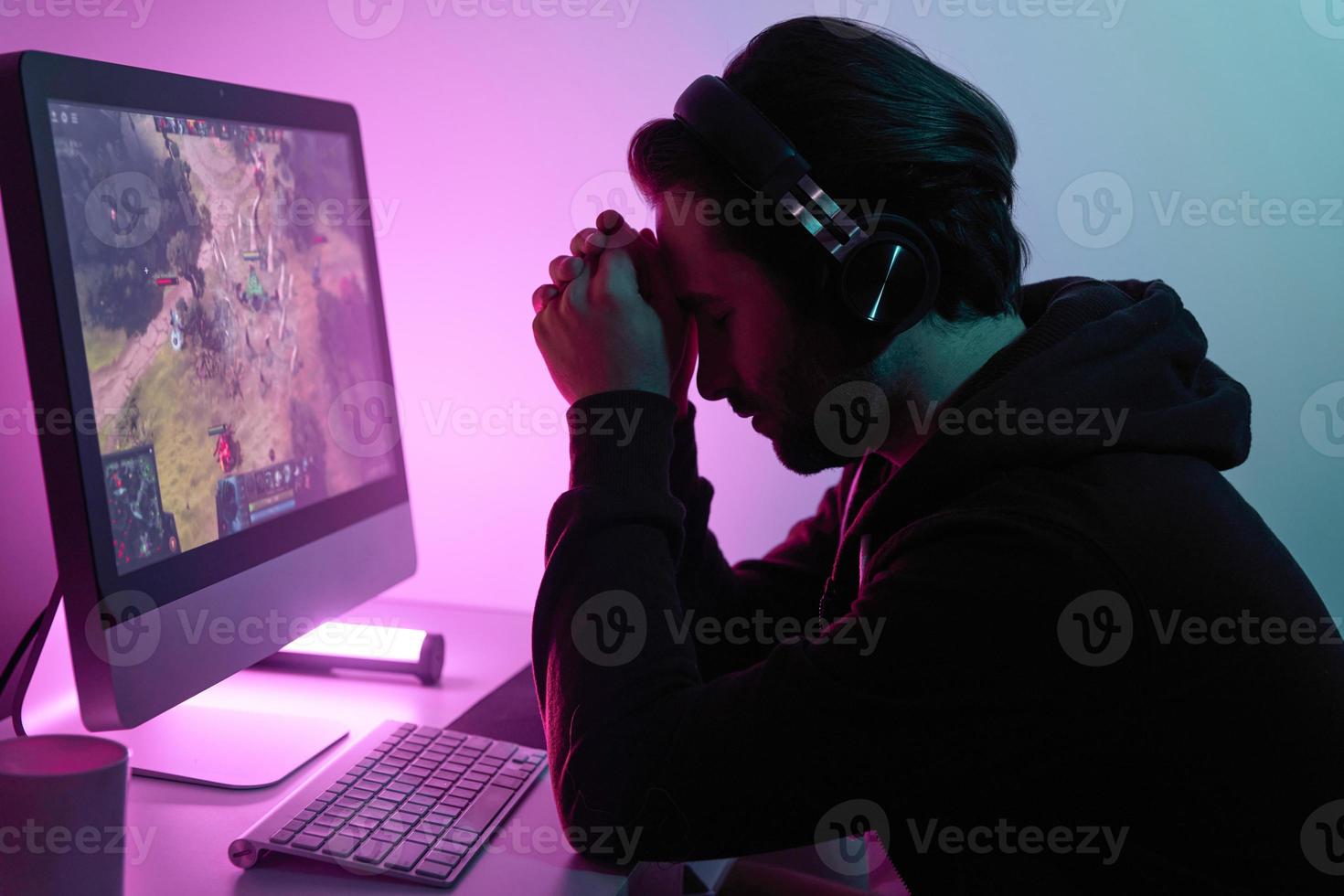 Frustrated young man leaning head on hands while playing game against colorful background photo