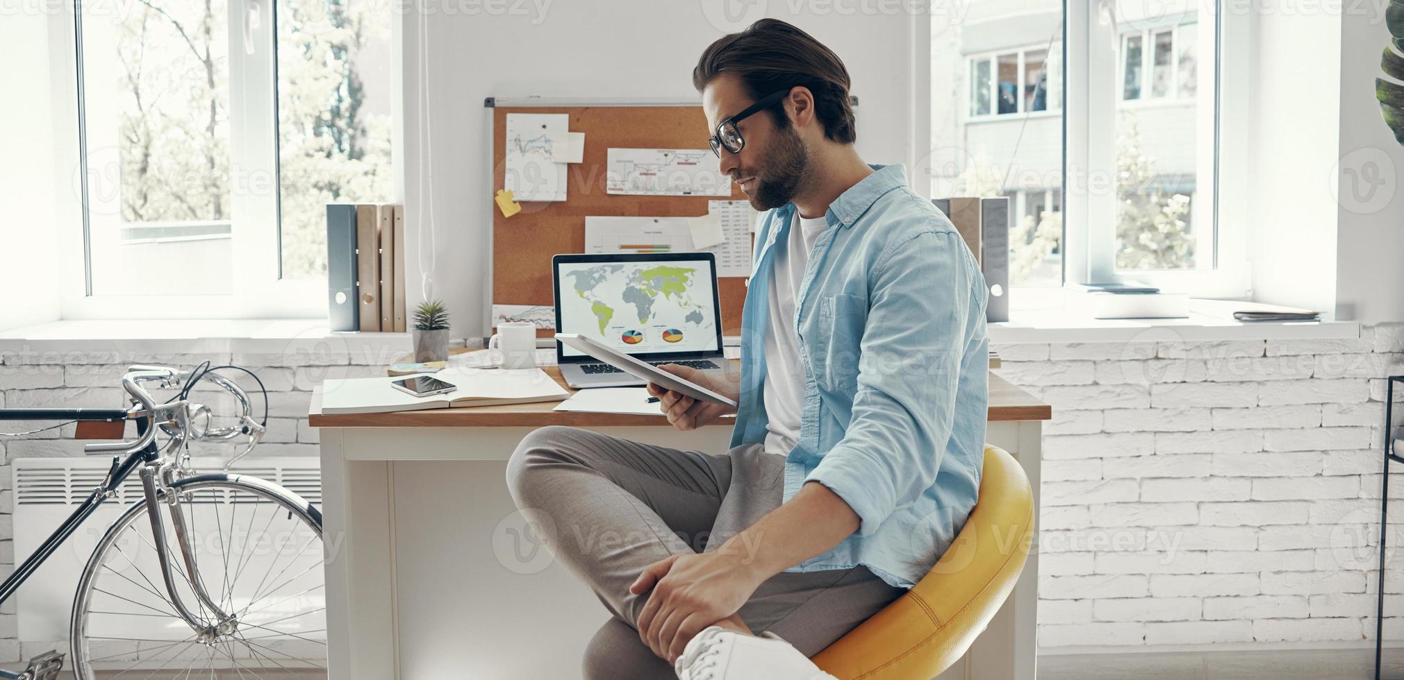 Handsome young man using digital tablet while sitting at his working place photo