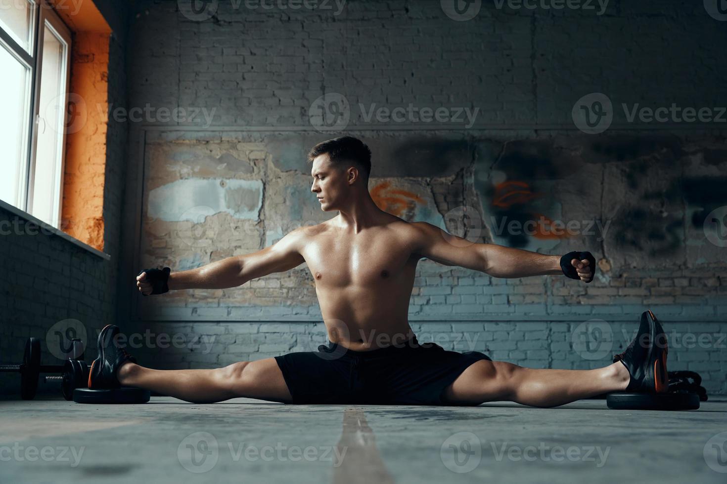 Confident young man doing the splits and keeping arms outstretched while exercising in gym photo