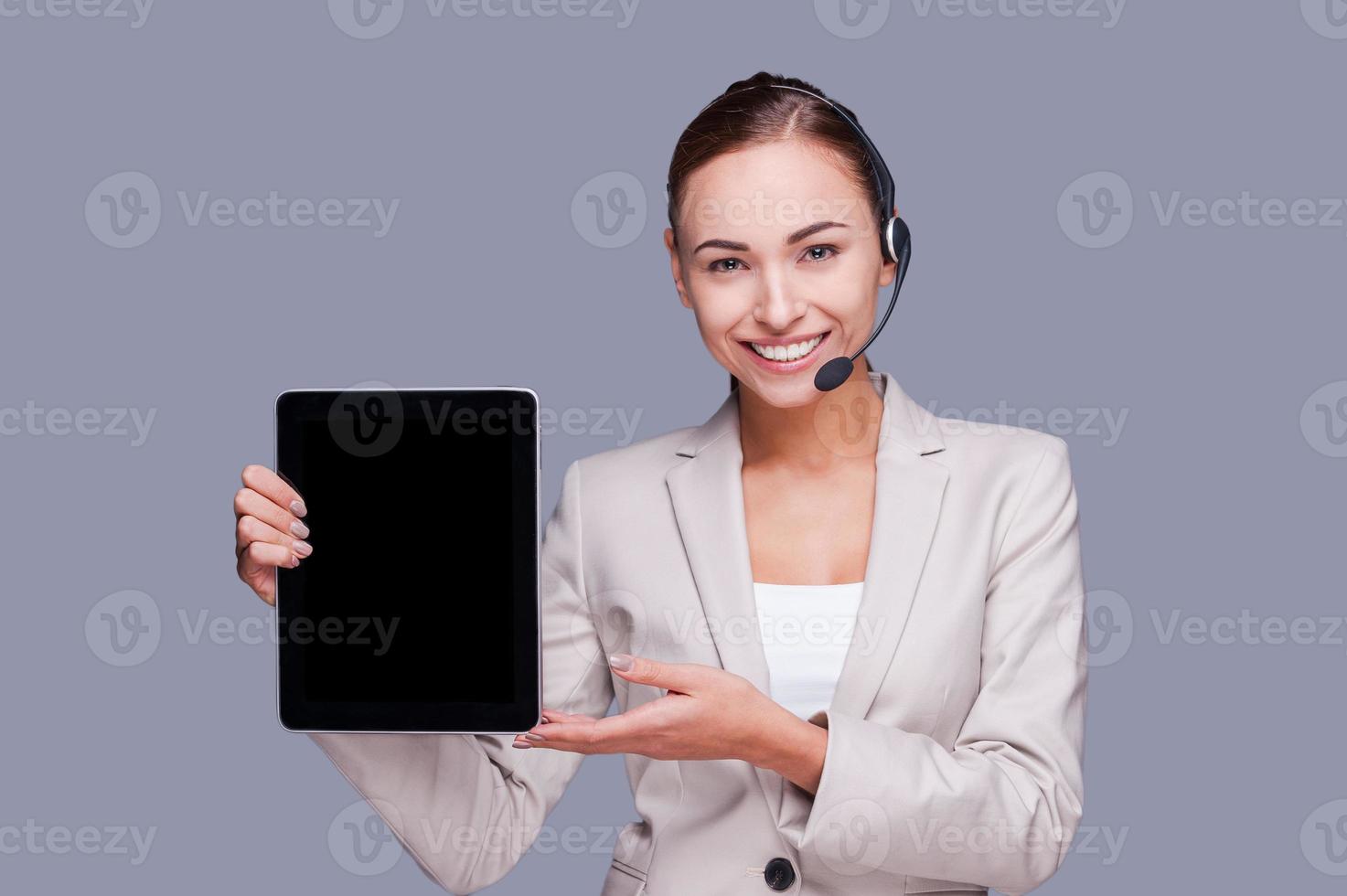 Copy space on her tablet. Confident young female operator holding digital tablet while standing against grey background photo