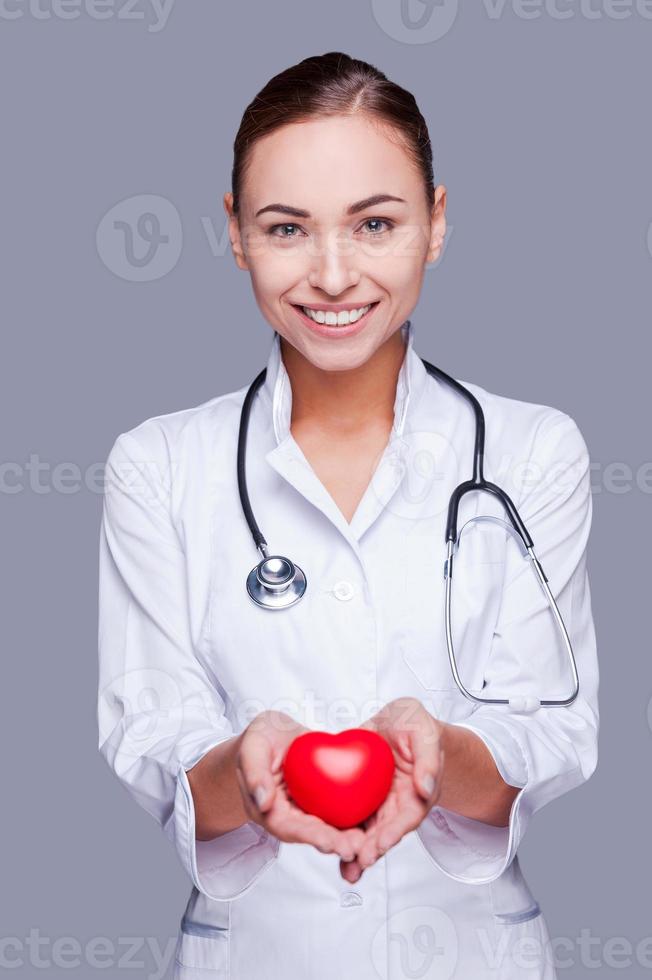 Your heart in good hands. Confident female doctor in white uniform holding heart prop and smiling photo