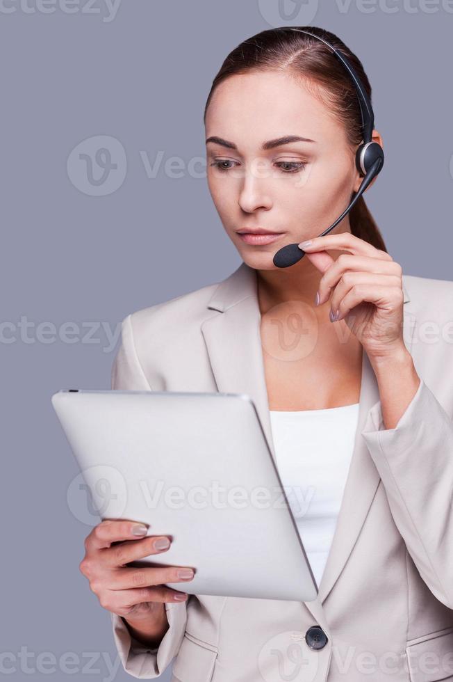 Busy at her work. Confident young customer service representative holding digital tablet while standing against grey background photo