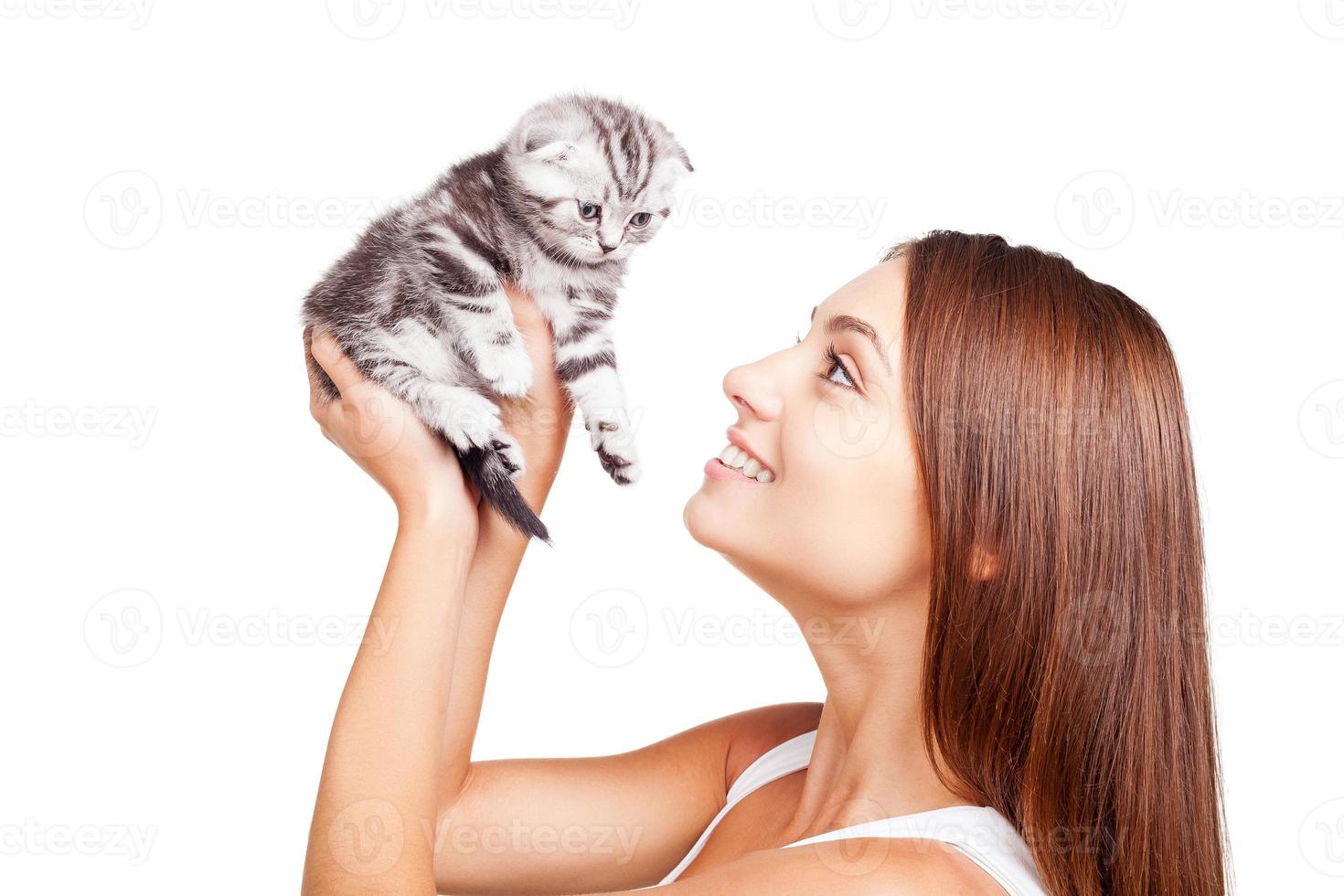 My little furry friend. Beautiful young woman holding little kitten in hands and looking at it with smile while standing isolated on white background photo