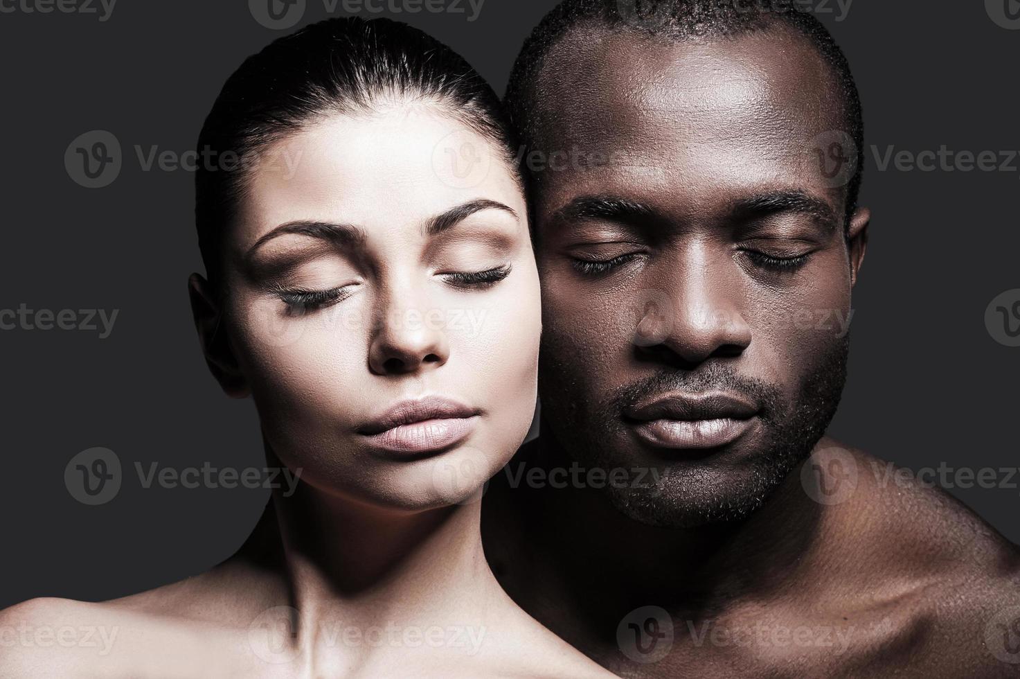 Face to face. Portrait of shirtless African man and Caucasian woman bonding their faces to each other and keeping eyes closed while standing against grey background photo