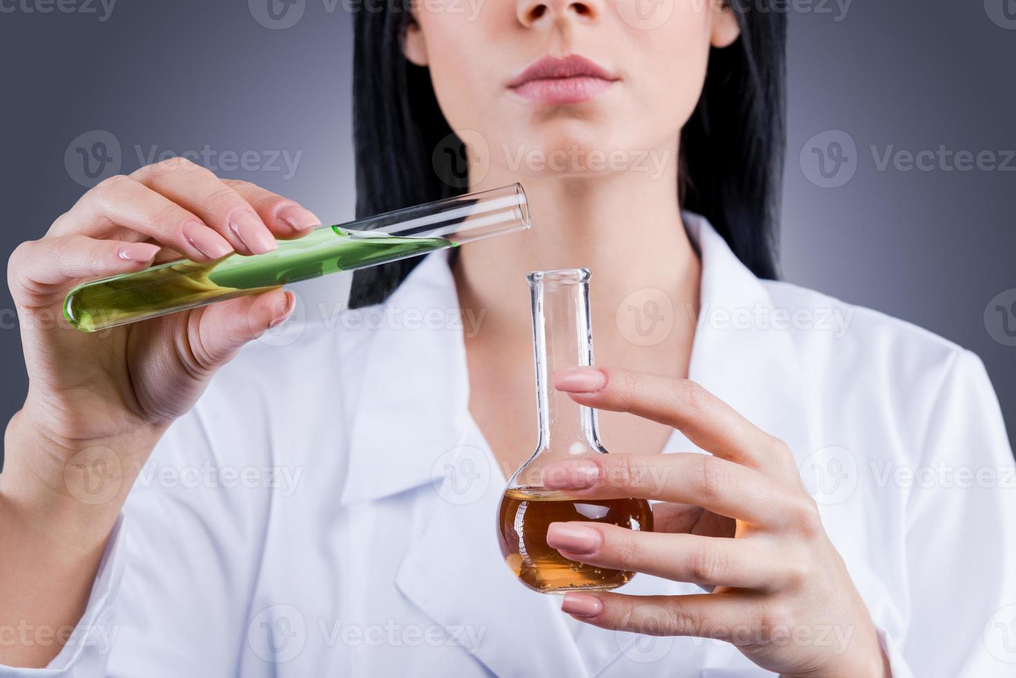 haciendo avanzar la medicina. primer plano de una doctora en uniforme blanco sosteniendo matraces mientras se enfrenta a un fondo gris foto