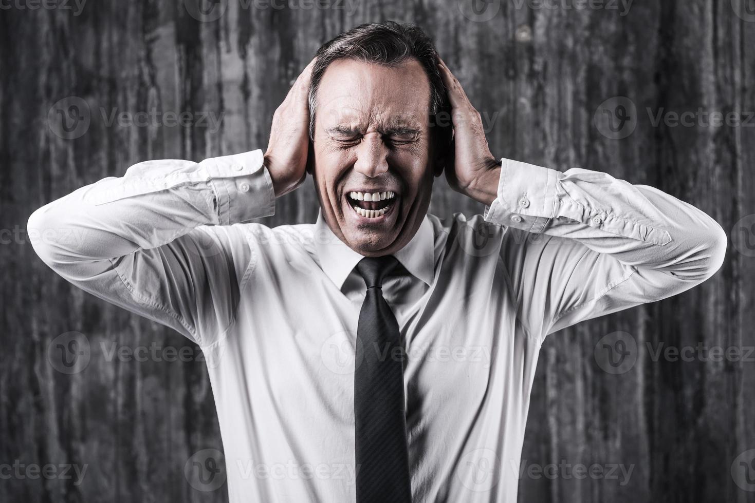 Emotional stress. Stressed mature man in shirt and tie holding head in hands and shouting while standing in front of dirty wall photo