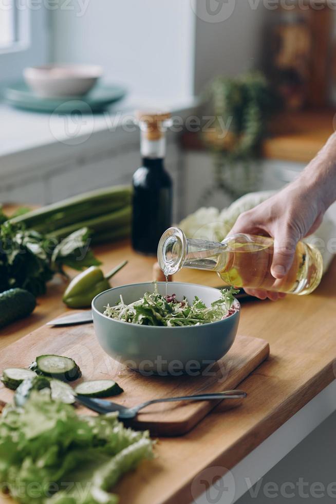 Close-up of unrecognizable man pouring olive oil into the bowl with fresh salad photo