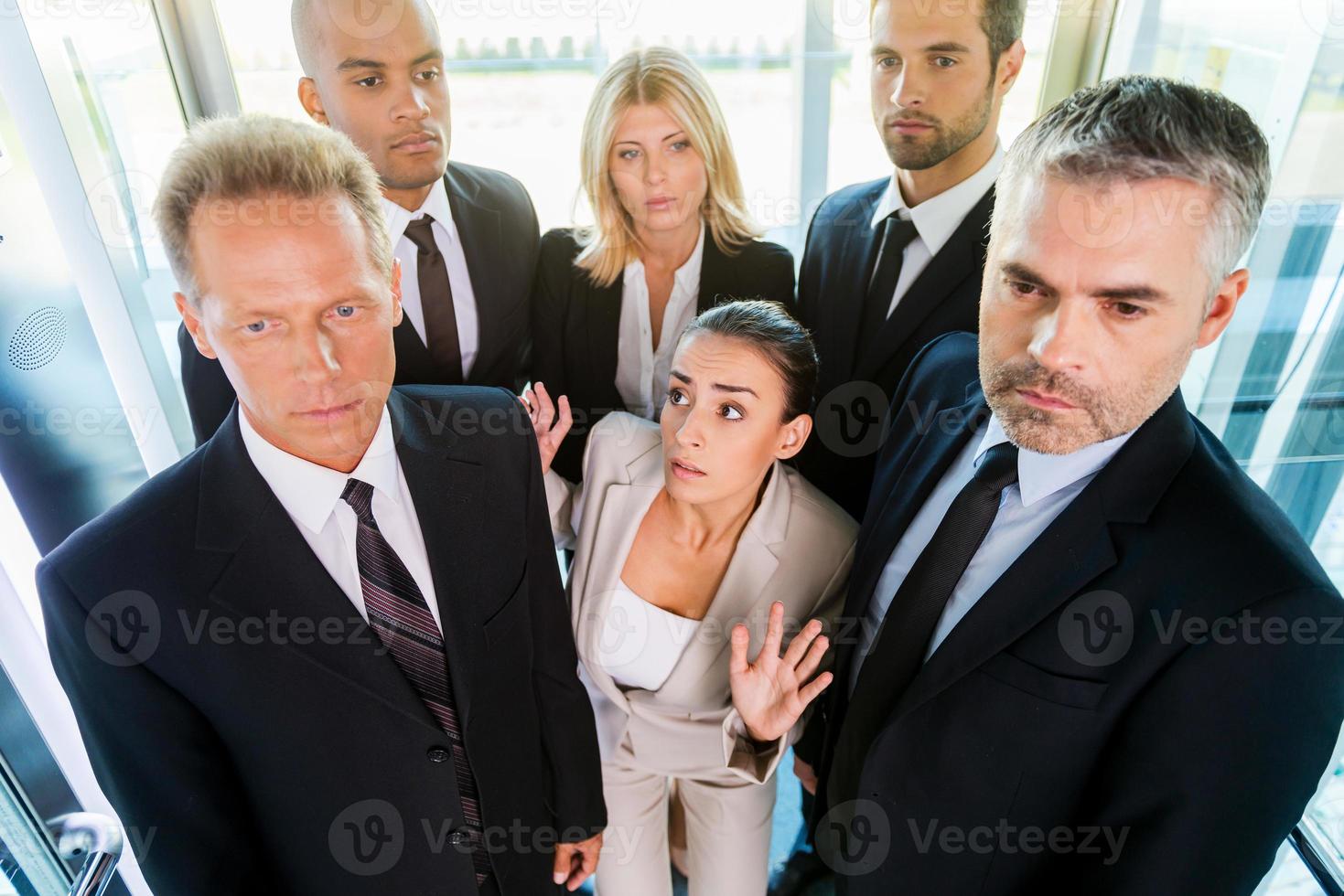 Drowning in people. Top view of fearful young woman in formalwear feeling trapped by the crowd while standing in elevator photo