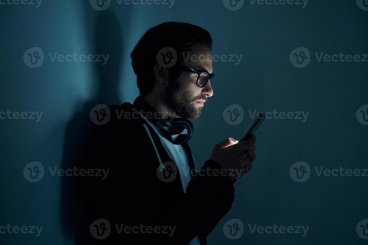 Confident young man using smart phone in the dark photo