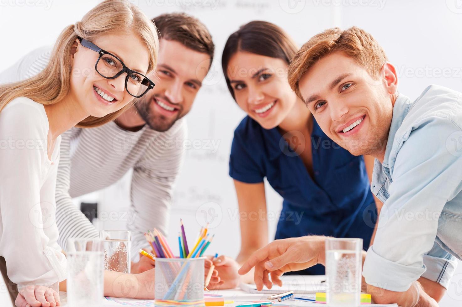 Young and creative team. Four cheerful business people in smart casual wear discussing something and smiling while leaning at the table photo