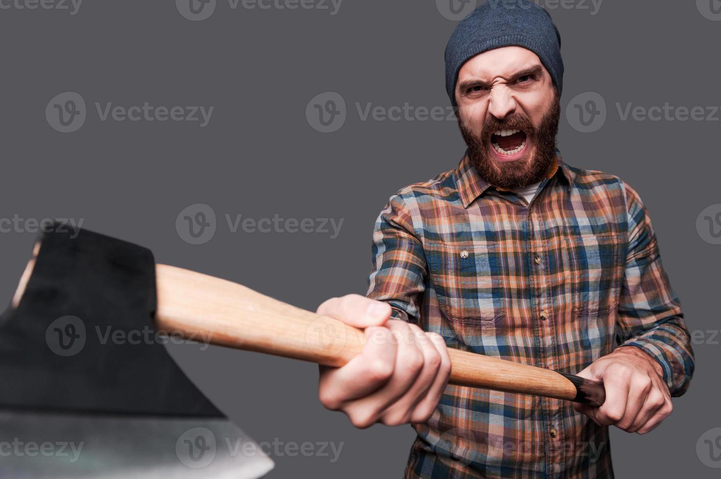 Taste my axe Furious young bearded man swinging his axe and shouting while standing against grey background photo