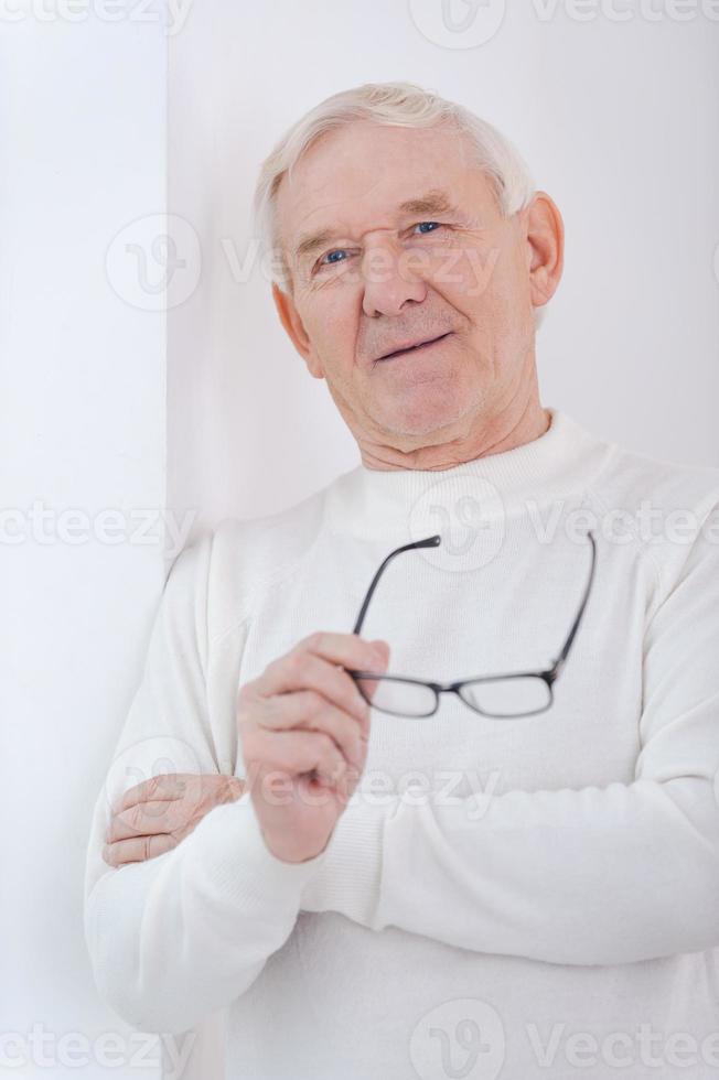 sabio guapo. un anciano alegre con los brazos cruzados y sonriendo a la cámara mientras se apoya en la pared foto