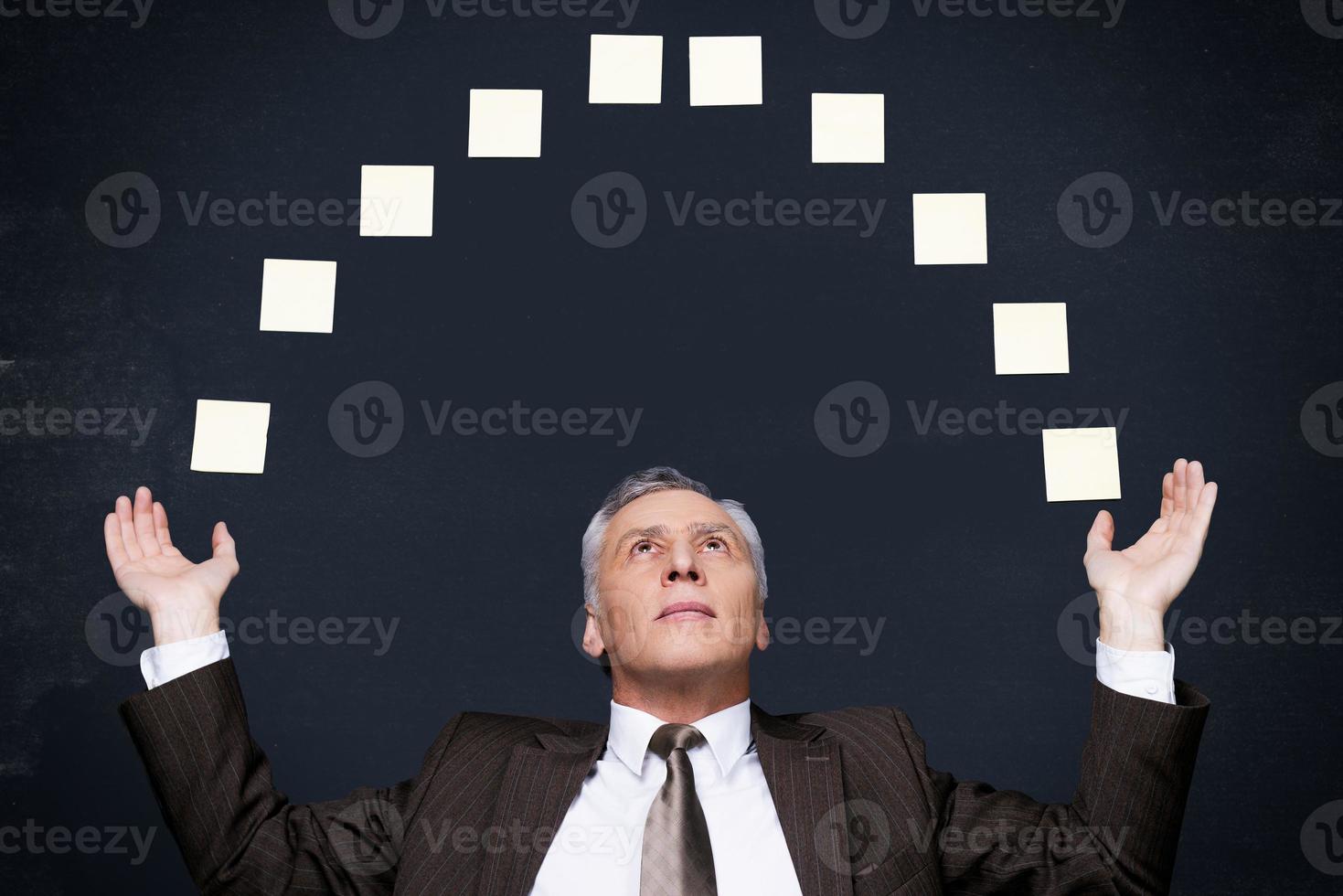 Businessman juggling. Confident senior man in formalwear juggling with adhesive notes while standing against blackboard photo