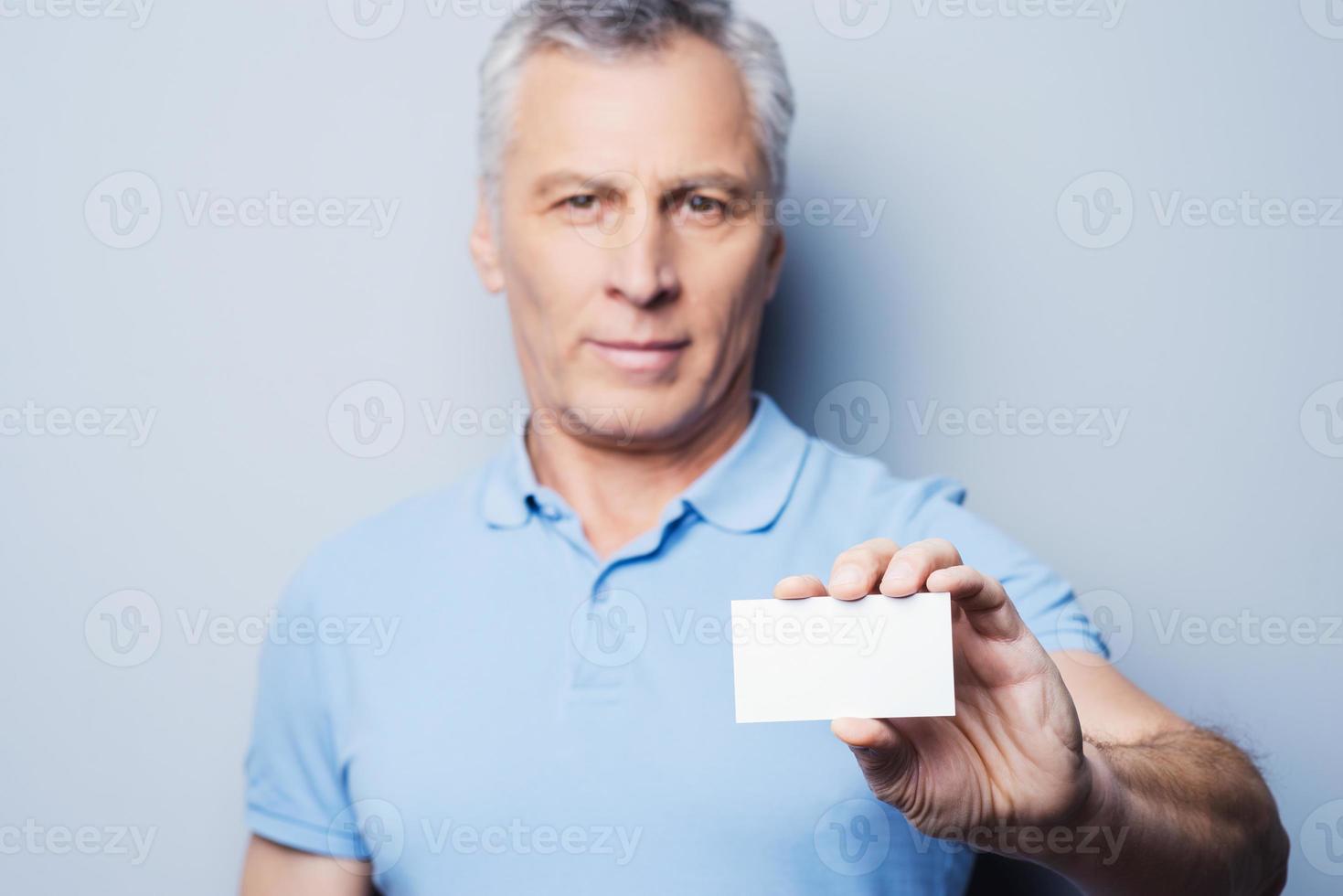 Call this number Handsome senior man stretching out a business card and smiling while standing against grey background photo
