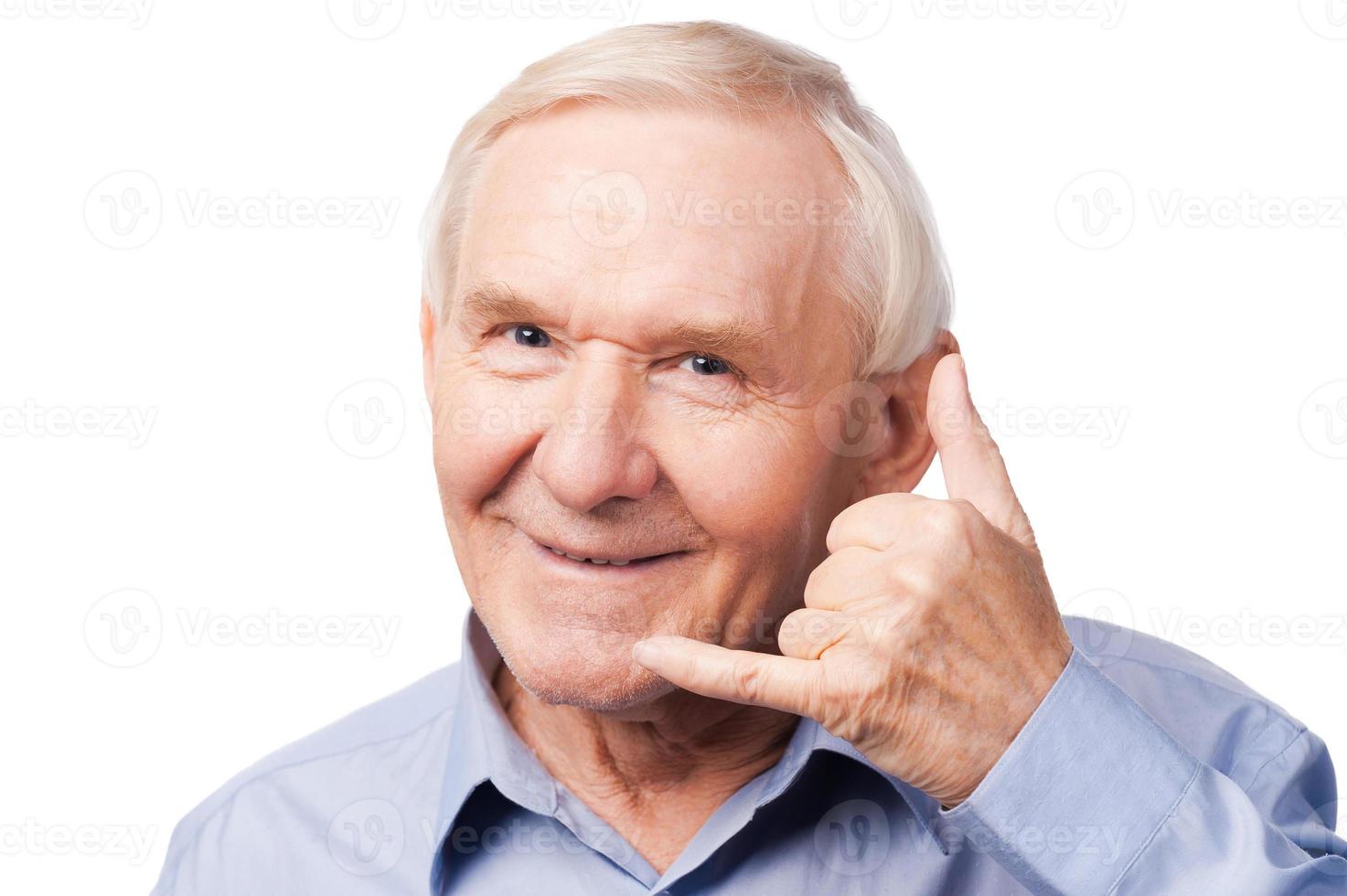 Waiting for your call. Cheerful senior man in shirt gesturing mobile phone near his face and smiling while standing against white background photo